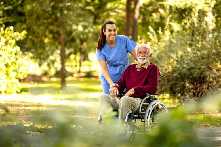 Older couple sitting together in a bright assisted living apartment while a caregiver reviews a daily routine.